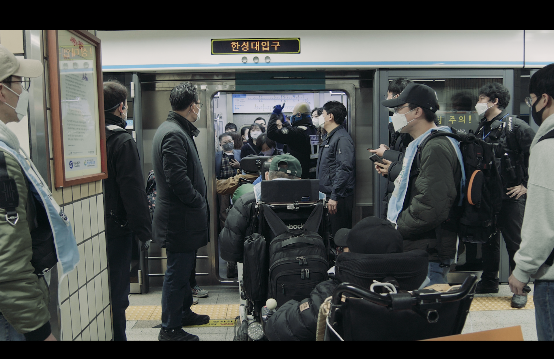 휠체어 이용 장애인 활동가들이 줄지어 출근길 지하철에 타고 있다. 지하철 문 위로 '한성대 입구' 역 명이 보인다.