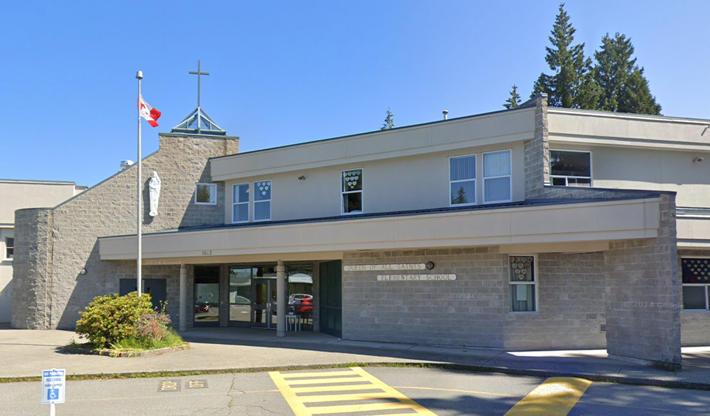 Photo of Queen of All Saints School. A frontal view of the school with a Canadian flag on a flag pole.