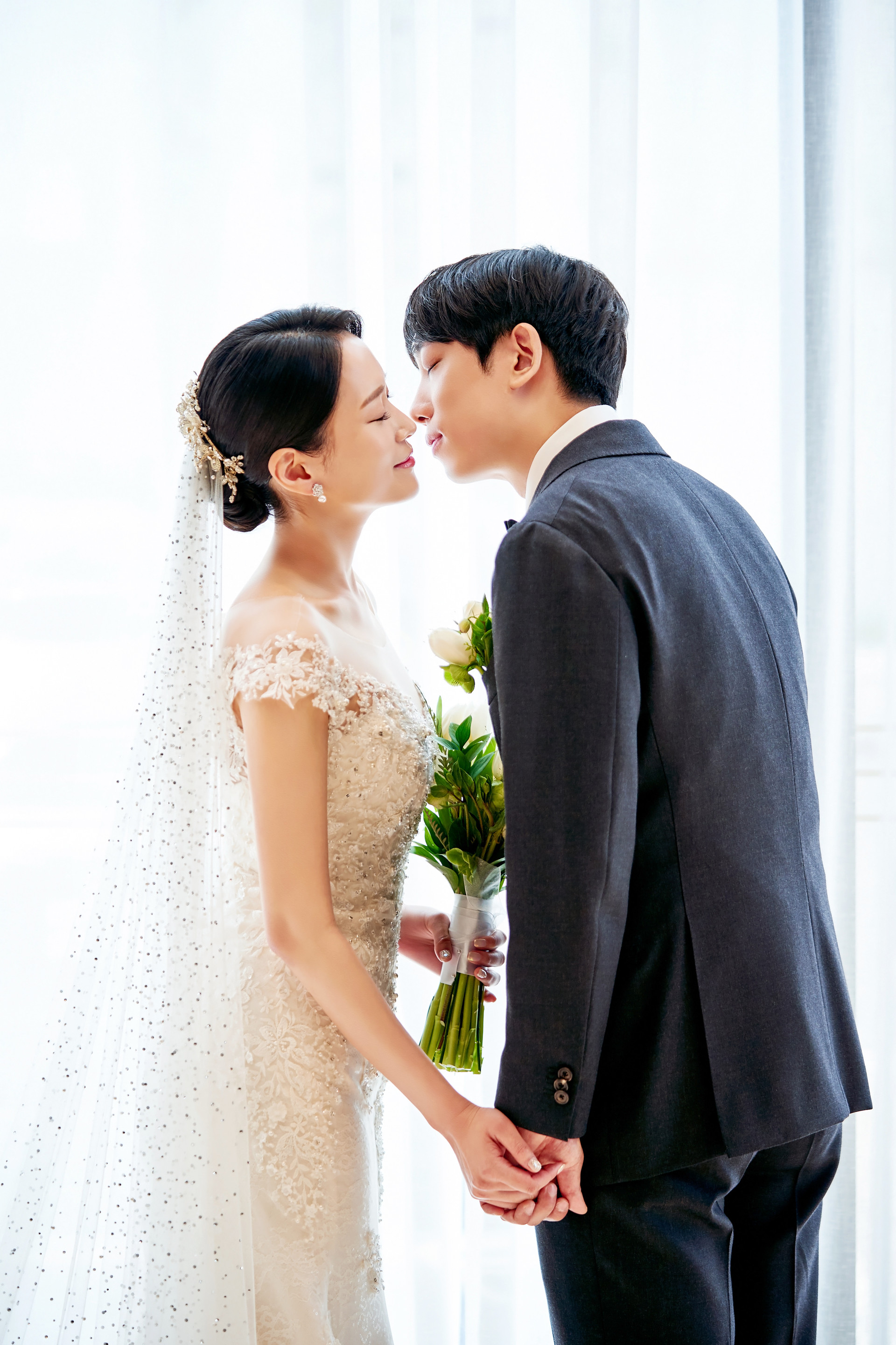 창가 빛 앞에서 손을 잡고 마주 선 신랑신부