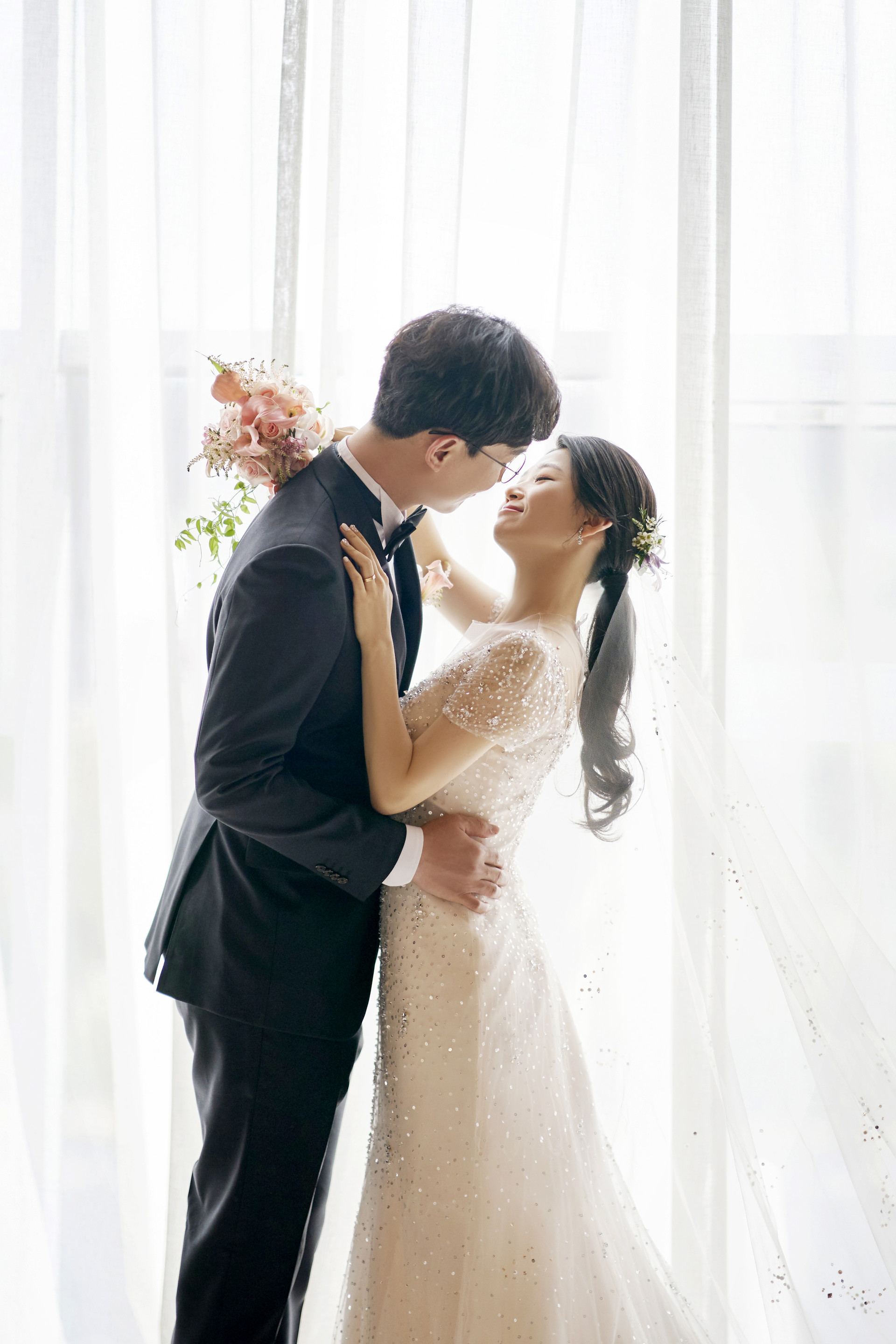 밝은 커튼 앞에서 이마를 맞대고 마주 선 신랑신부