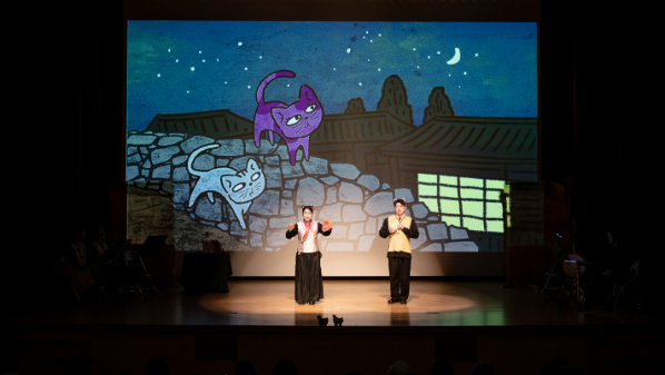 "나는 고양이로소이다 공연 무대 위에 밤하늘과 고양이 일러스트가 등장하고 두 배우가 공연하는 모습"