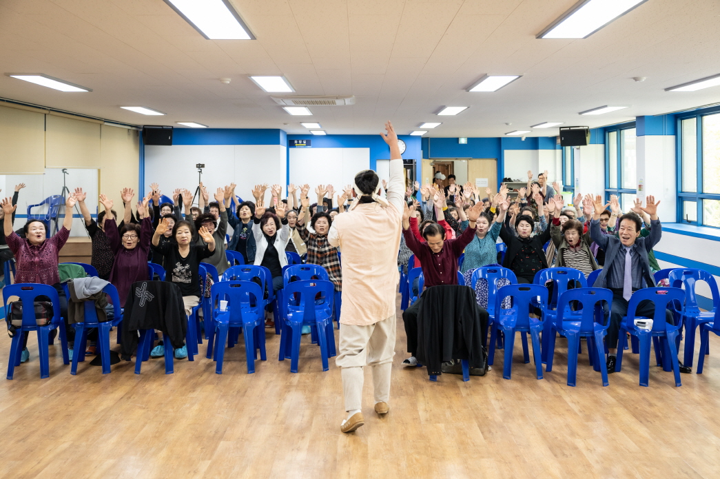 무대 앞에서 연희자가 어르신들과 함께 손을 높이 들며 ‘복을 부르는 동작’을 유도하는 장면