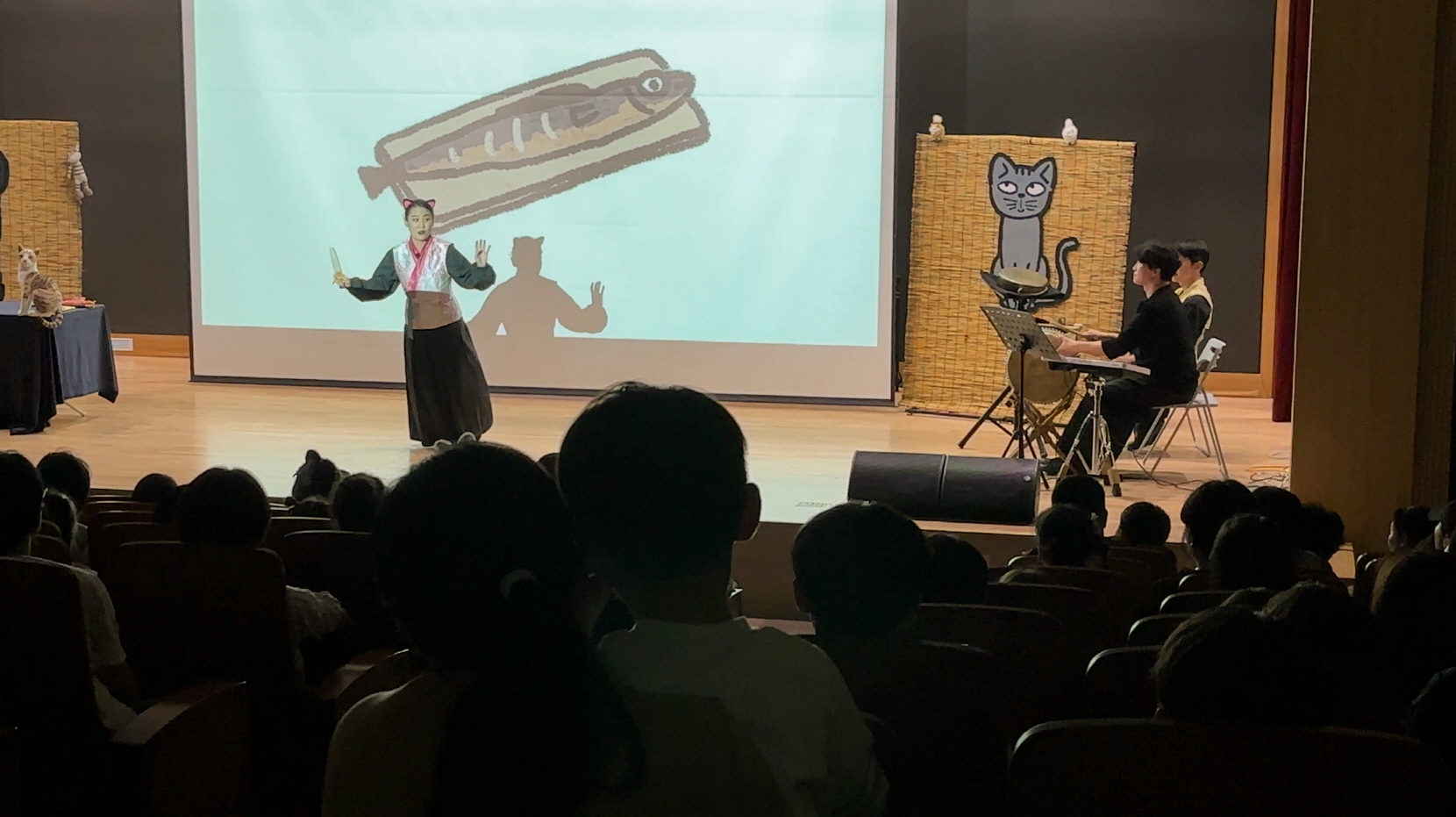 충남도서관 나는 고양이로소이다 공연 중 고양이 분장의 배우가 아이들과 소통하며 연기하고, 전통 타악 연주자들이 무대를 함께하는 모습