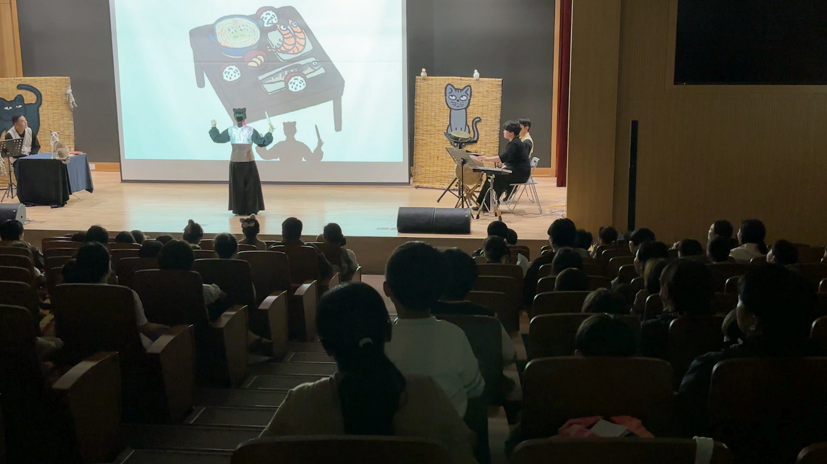 충남도서관 나는 고양이로소이다 공연 중, 무릎 위에 아이를 안고 함께 무대를 바라보는 엄마의 모습과 몰입한 객석 분위기