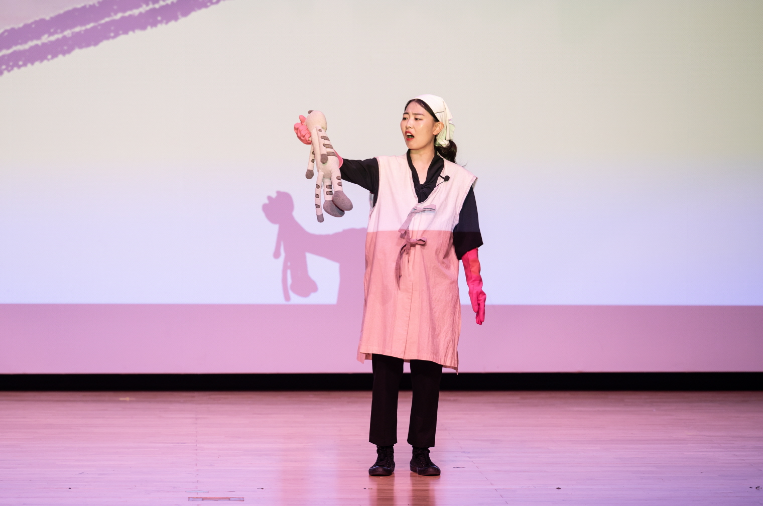 어린이 마당놀이 〈나는 고양이로소이다〉 공연 중, 주인공 고양이가 새 가족에게 입양된 후 매일 사고를 쳐서 혼나는 장면. 분홍 고무장갑을 낀 새 가족 역할의 배우가 고양이 인형을 들고 화난 표정으로 꾸짖고 있으며, 무대에는 인형의 그림자가 크게 비춰진다.