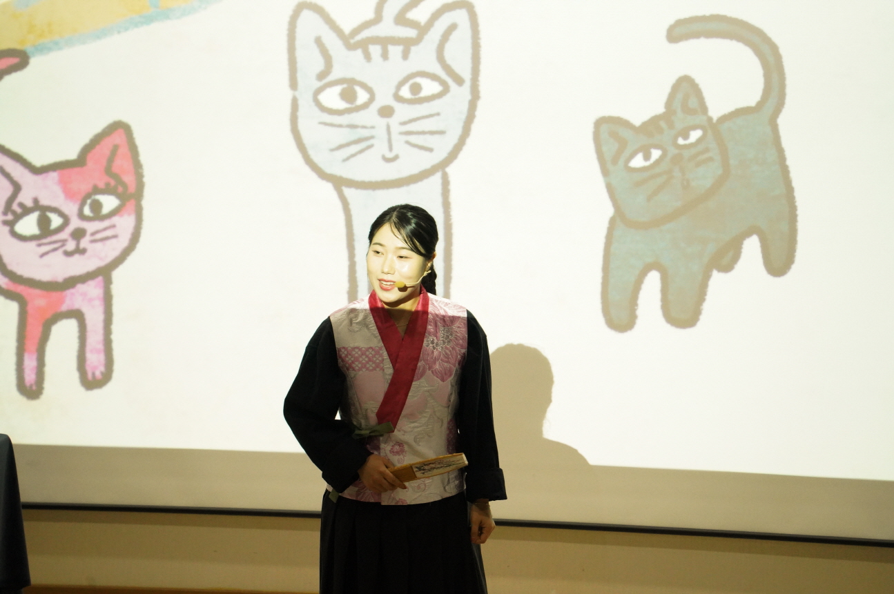 순천 기적의도서관에서 열린 어린이 마당놀이 ‘나는 고양이로소이다’ 공연 중, 고양이 일러스트 배경 앞에서 이야기하는 여성 배우.