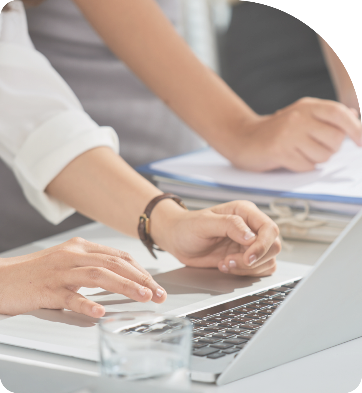 책상 위에서 노트북을 사용하며 함께 작업하는 두 사람의 손을 근접 촬영한 이미지. 한 사람은 키보드를 입력하고, 다른 사람은 서류 위에서 펜으로 가리키며 설명하고 있다.