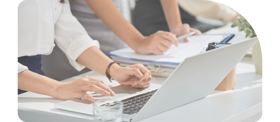 책상 위에서 노트북을 사용하며 함께 작업하는 두 사람의 손을 근접 촬영한 이미지. 한 사람은 키보드를 입력하고, 다른 사람은 서류 위에서 펜으로 가리키며 설명하고 있다.