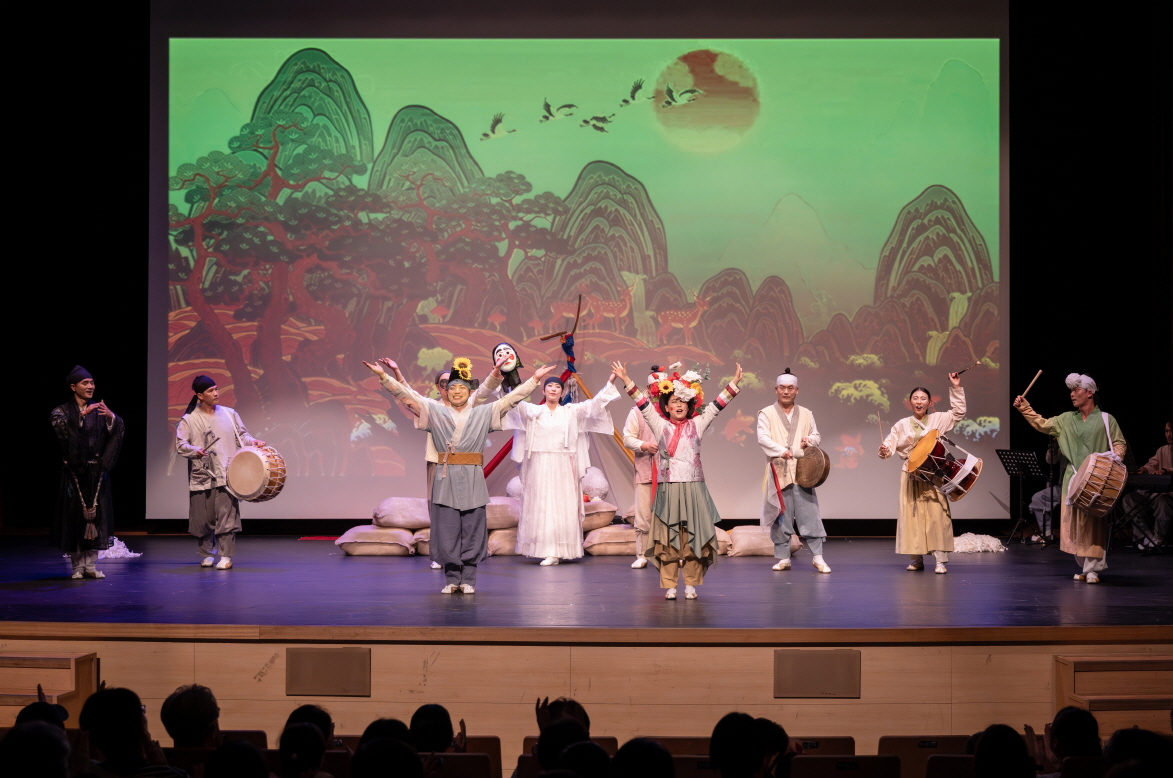 전통 마당놀이 지신지신 무대에서 배우들이 모두 함께 손을 들고 관객과 교감하며 피날레 장면을 연출하는 모습, 배경에는 산수화풍의 병풍 영상이 비춰지는 장면