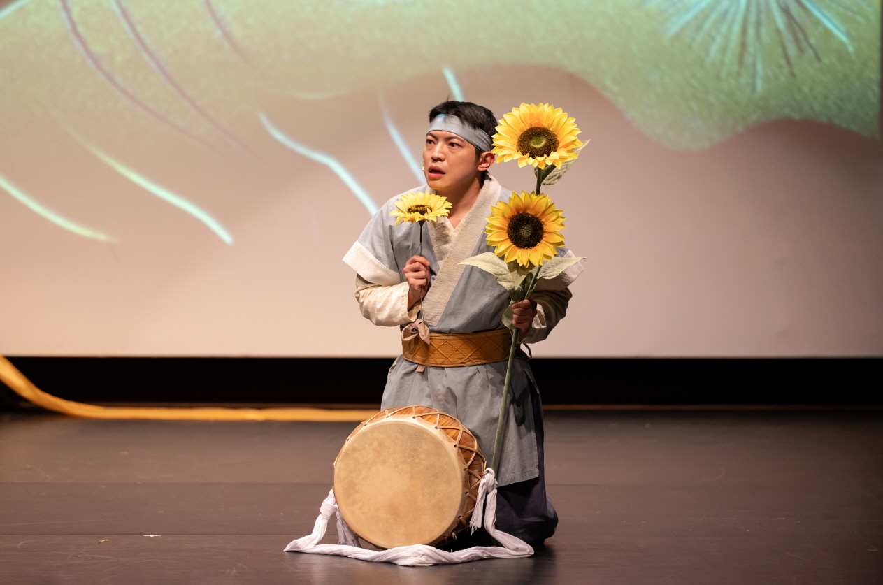마당놀이 지신지신 무대 위에서 장구에앉아 해바라기를 들고 고백할 기회를 기다리는 코믹한 배우의 모습,.