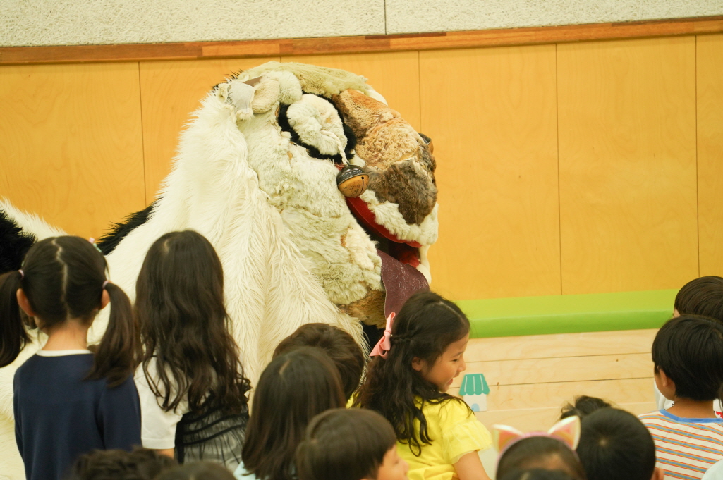 전주아름유치원에서 열린 유치원 공연 ‘풍물마당놀이 해피’ 중, 강아지 탈을 쓴 해피가 아이들 곁에 다가와 앉아있고 아이들이 호기심 어린 눈빛으로 바라보며 웃는 모습