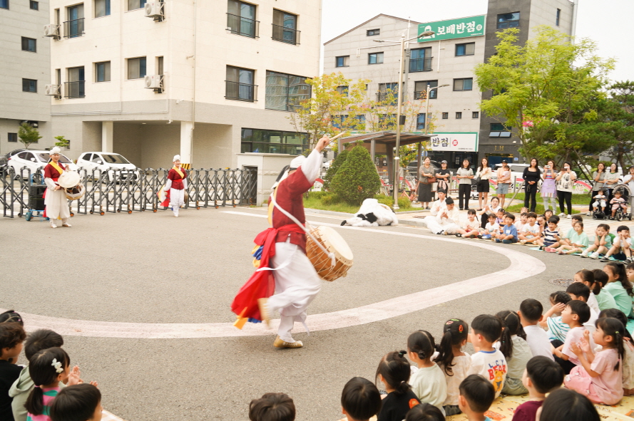 서산예천새뜰유치원 공연에서 풍물패가 우스꽝스로운 동작으로 북춤을 추며 흥겹게 공연하고 아이들이 즐겁게 관람하는 모습, 전통 공연 풍물마당놀이 해피