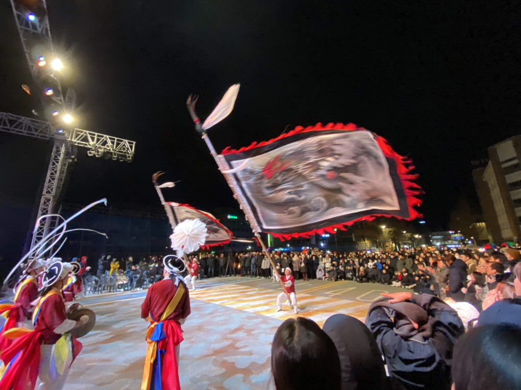 야외 국제행사 공연,합굿마을 전통연희단이 야간 무대에서 대형 용깃발을 휘두르며 기접놀이 공연을 펼치고, 수많은 관객이 한국 전통문화를 즐기는 모습
