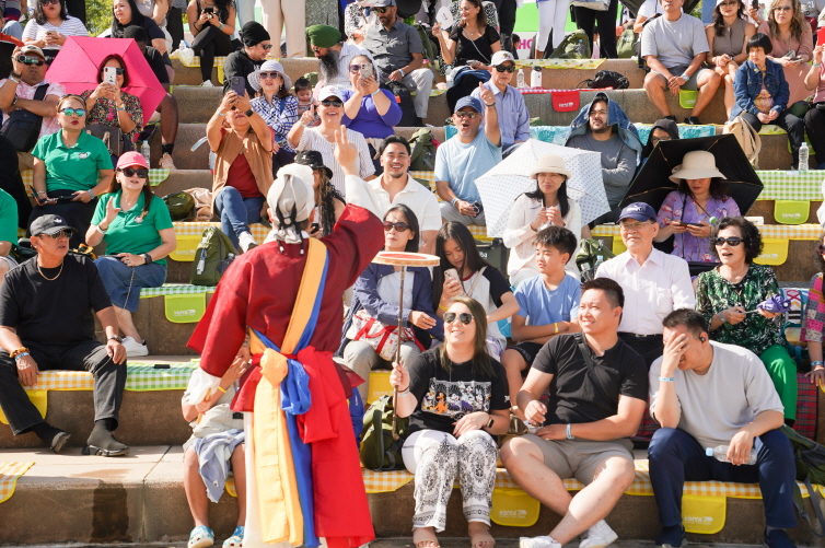 여의도 한강공원 WSB K-DAY 국제행사에서 합굿마을 연희단과 외국인 관객이 함께 접시돌리기 체험을 즐기며 웃음과 호응을 나누는 전통연희 공연 장면