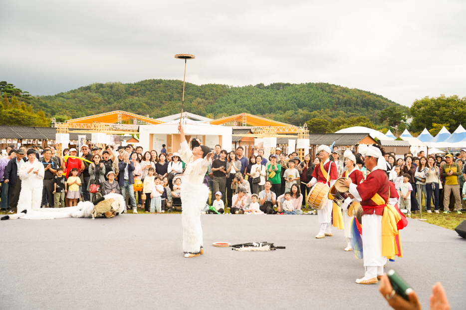 2025 안성 바우덕이 축제 풍물마당놀이 해피 공연에서 출연자가 버나놀이를 선보이며 접시를 막대 위에 돌리는 전통 묘기를 펼치자 관객들이 환호하는 장면