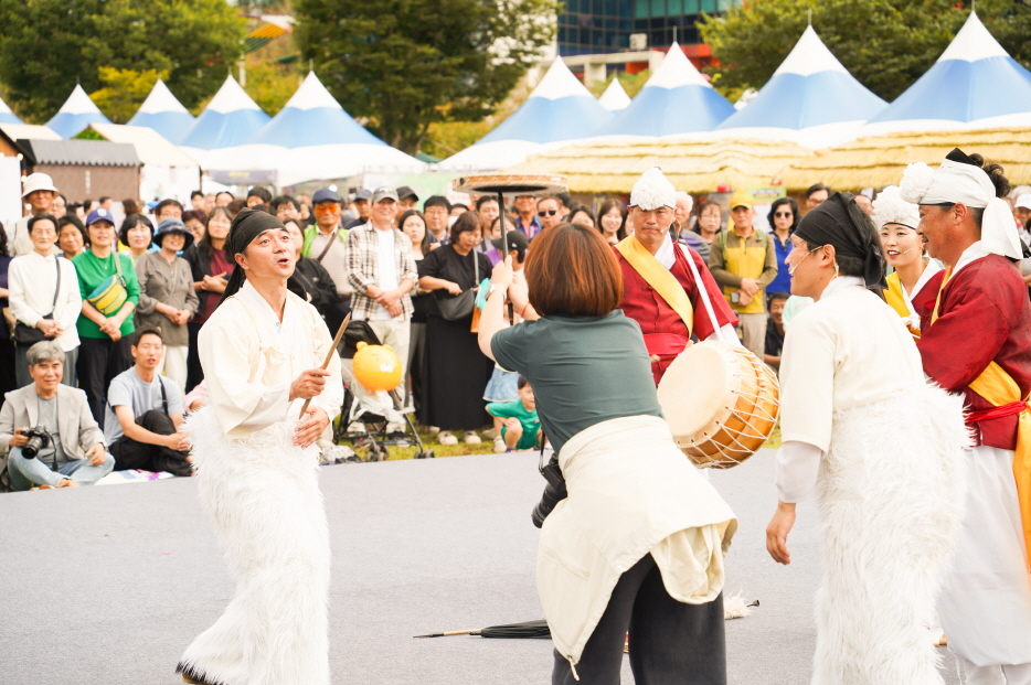 2025 안성 바우덕이 축제 풍물마당놀이 해피 공연에서 관객이 무대에 올라 버나놀이 접시돌리기 묘기에 직접 참여하며 출연자들과 즐겁게 소통하는 장면