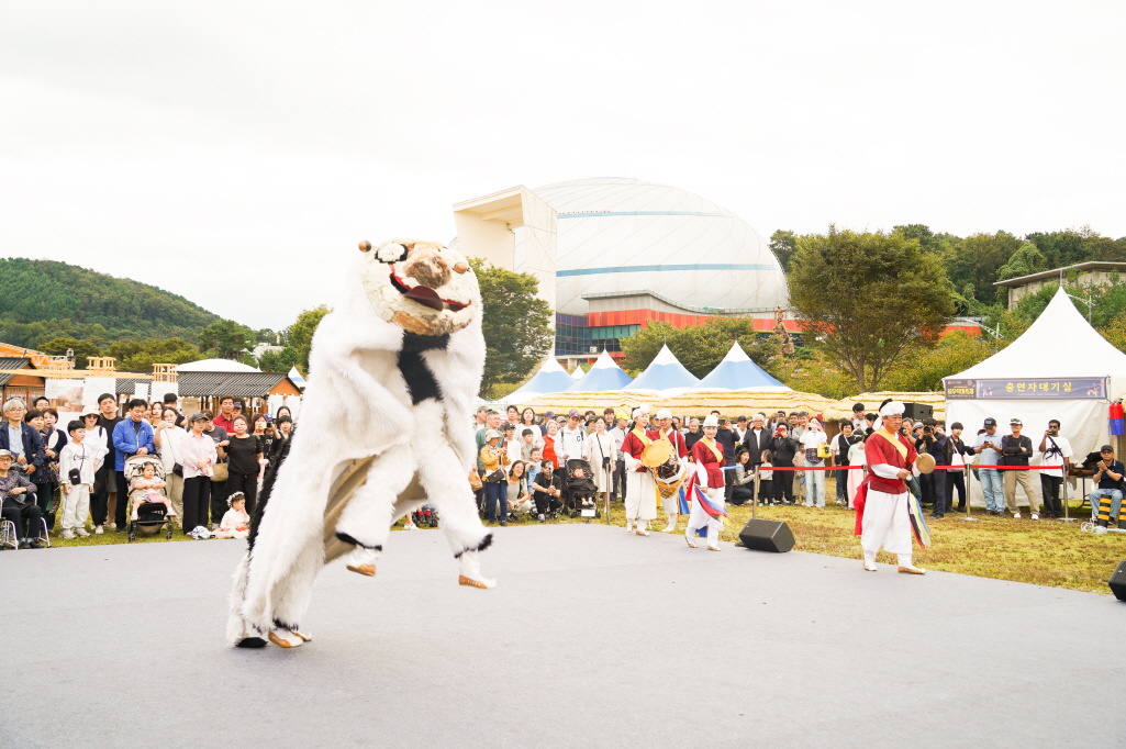 2025 안성 바우덕이 축제 에서 합굿마을의 풍물마당놀이 해피 공연에서 거대한 강아지 탈 캐릭터가 무대 위에서 역동적으로 뛰어오르며 사자탈춤을 추는  전통 공연 장면