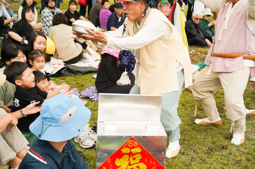2025 안성 바우덕이 축제 마당놀이 복이팡팡 공연에서 출연자가 복 상자를 열고 떡을 나누며 아이들과 관객에게 자손복을 전하는 장면