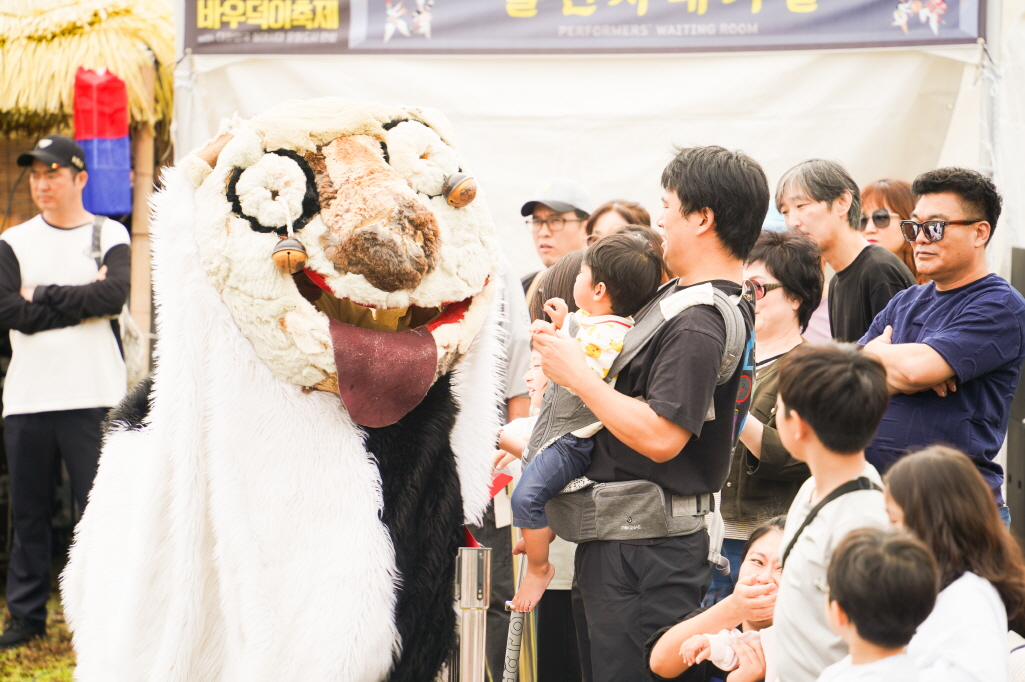 안성 바우덕이 축제 2025 현장에서 풍물마당놀이 해피 공연의 귀여운 강아지 탈이 관객들과 만나는 장면, 아이와 가족들이 탈 캐릭터를 보고 즐거워하는 모습
