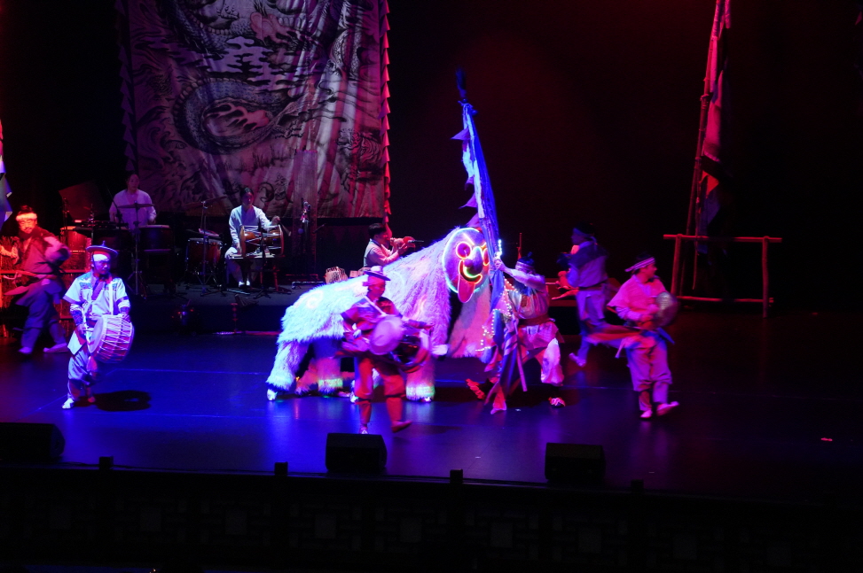 마당놀이 용을쫓는사냥꾼 공연의 LED 쇼 장면으로, 사자탈이 형형색색의 LED 를 빛내며  등장하고, 연희자들이 용 깃발과 북, 장구를 들고 무대를 신명나게 누비는 모습