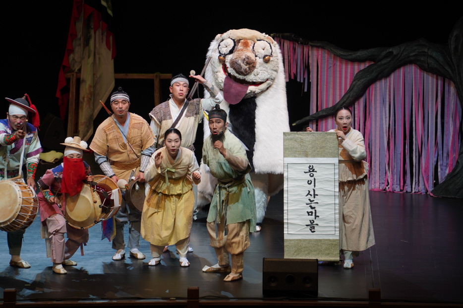 마당놀이 용을쫓는사냥꾼 공연 중 출연진과 강아지 해피가 '용이 사는 마을'  앞에서 포즈를 취하며 관객을 바라보는 장면