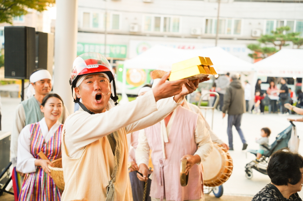 합굿마을 연희단 배우가 금괴 소품을 들고 복을 나누는 어르신 마당놀이 복이팡팡 공연 장면