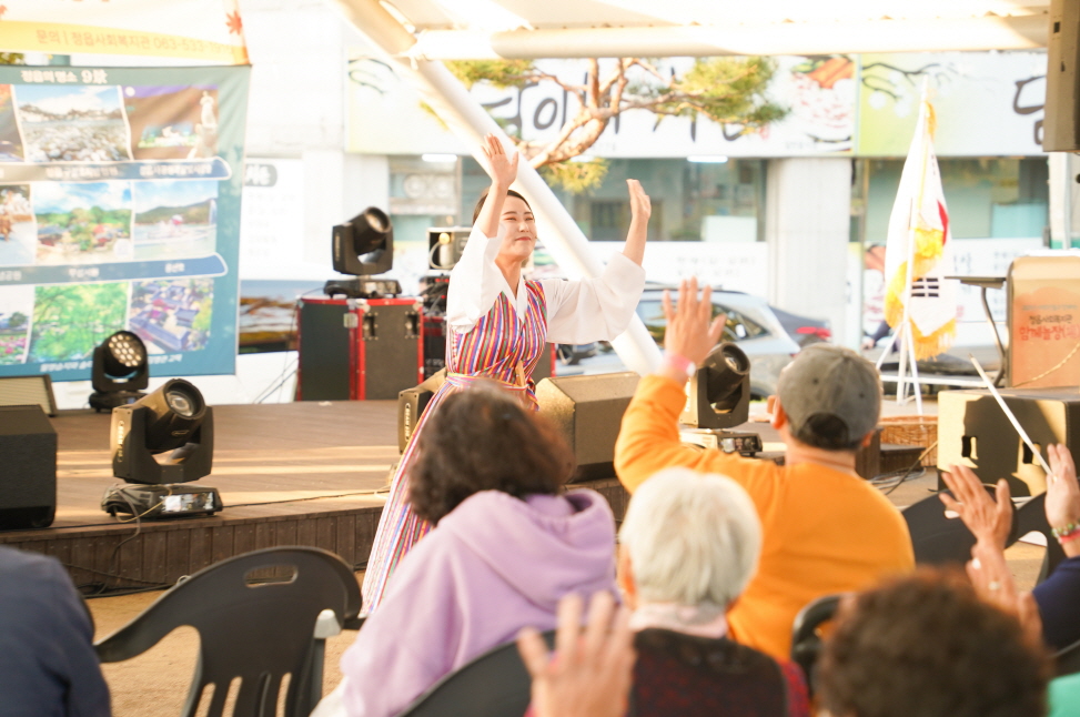 복이팡팡 공연에서 합굿마을 연희단 배우가 무대 아래에서 어르신 관객들과 함께 손을 들며 소통하는 장면