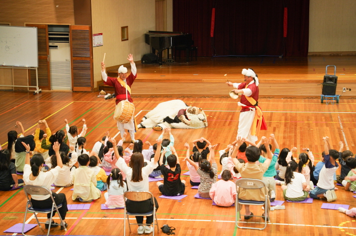 풍물마당놀이 해피 공연에서 풍물단이 장단을 맞추며 해피를 부르는 장면, 아이들이 손을 들고 함께 노동요 합창하며 응원하는 모습｜조치원 대동병설유치원 전통공연