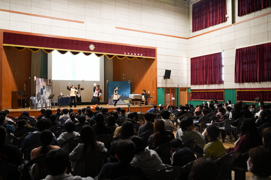 광주 오치초등학교 강당에서 열린 어린이 마당놀이 ‘나는 고양이로소이다’ 공연을 관람하는 학생들 — 무대에서 배우들이 연기하고 객석의 어린이들이 집중하는 모습