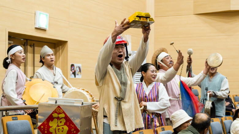 어르신 마당놀이 ‘복이 팡팡’에서 연희패가 금덩어리 소품을 들고 객석으로 들어와 어르신들과 함께 장단을 나누며 호응을 이끌어내는 장면, 한국전통문화전당 공연장