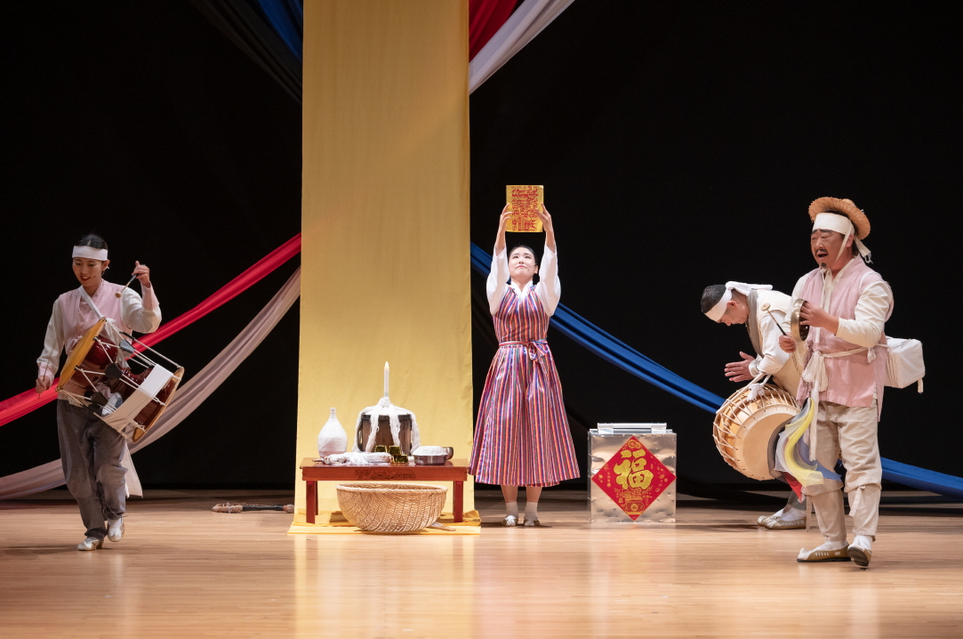 어르신 마당놀이 ‘복이 팡팡’ 무대에서 연희자가 복 부적을 높이 들고 고사상 앞에서 의례 장면을 연출하고, 장구·꽹과리 장단이 함께 어우러지는 한국 전통 연희 공연