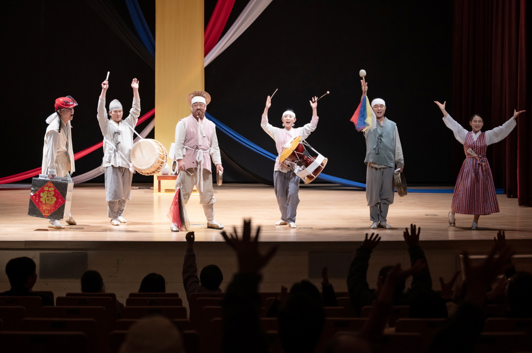 “어르신 마당놀이 ‘복이 팡팡’ 피날레 장면에서 연희패가 두 팔을 올리고 장단을 울리며 관객과 함께 호응하는 모습, 객석에서도 손을 들며 화답하는 한국 전통 공연