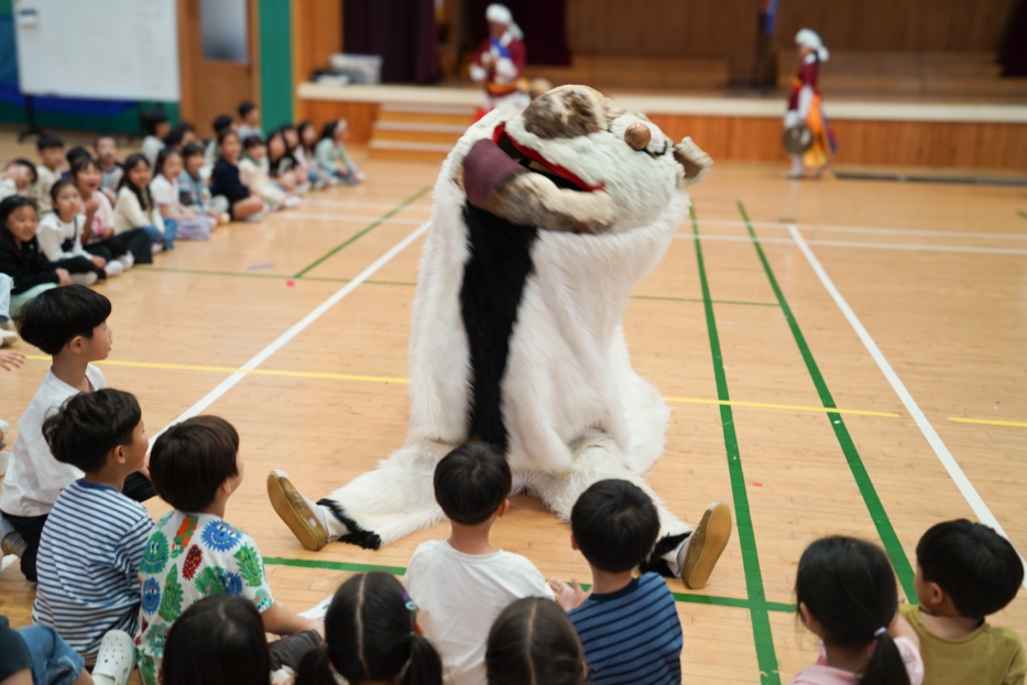 유치원 강당에서 강아지탈 해피가 아이들 앞에서 눈높이를 맞추며 교감하는 체험형 전통공연 풍물마당놀이 해피