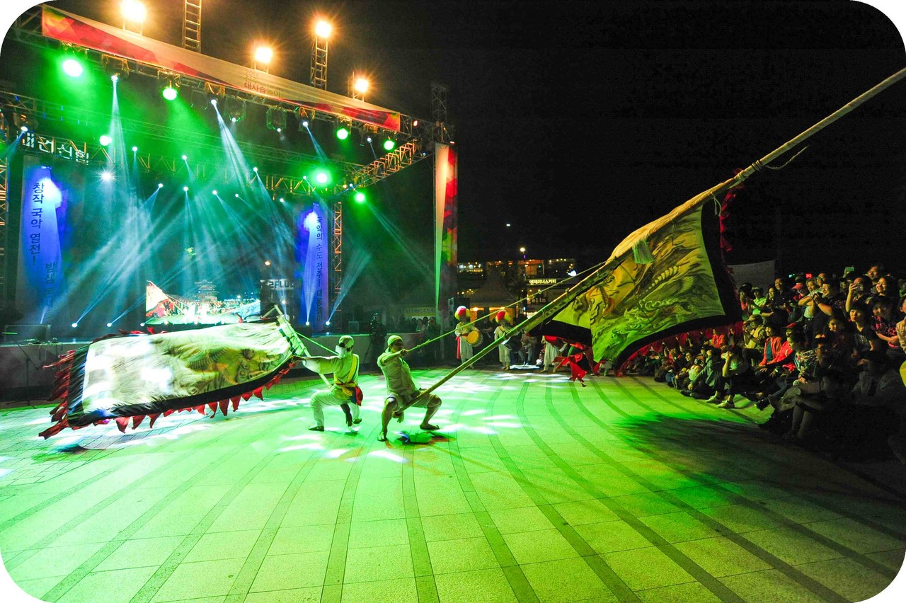 주한옥마을 특설무대에서 열린 전주대사습놀이 폐막초청공연 중 화려한 녹색 조명 아래 두 명의 연희자가 대형 용깃발을 낮게 휘두르며 기예를 펼치는 합굿마을 기접의 역동적인 무대 장면