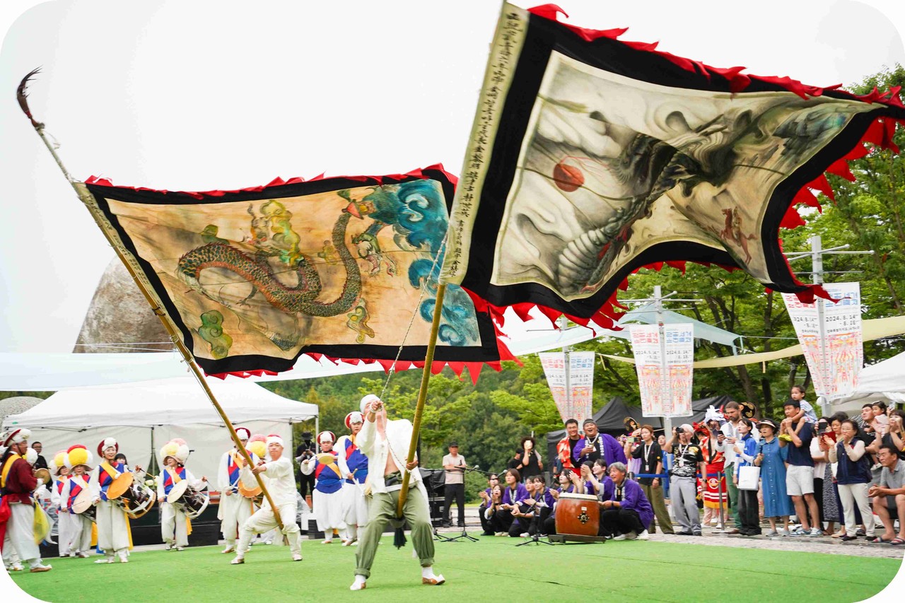 전주세계소리축제 야외 잔디 무대에서 두 개의 대형 용깃발이 교차하며 웅장한 기상을 뽐내는 글로벌 문화 예술 교류 한일협력공연 현장