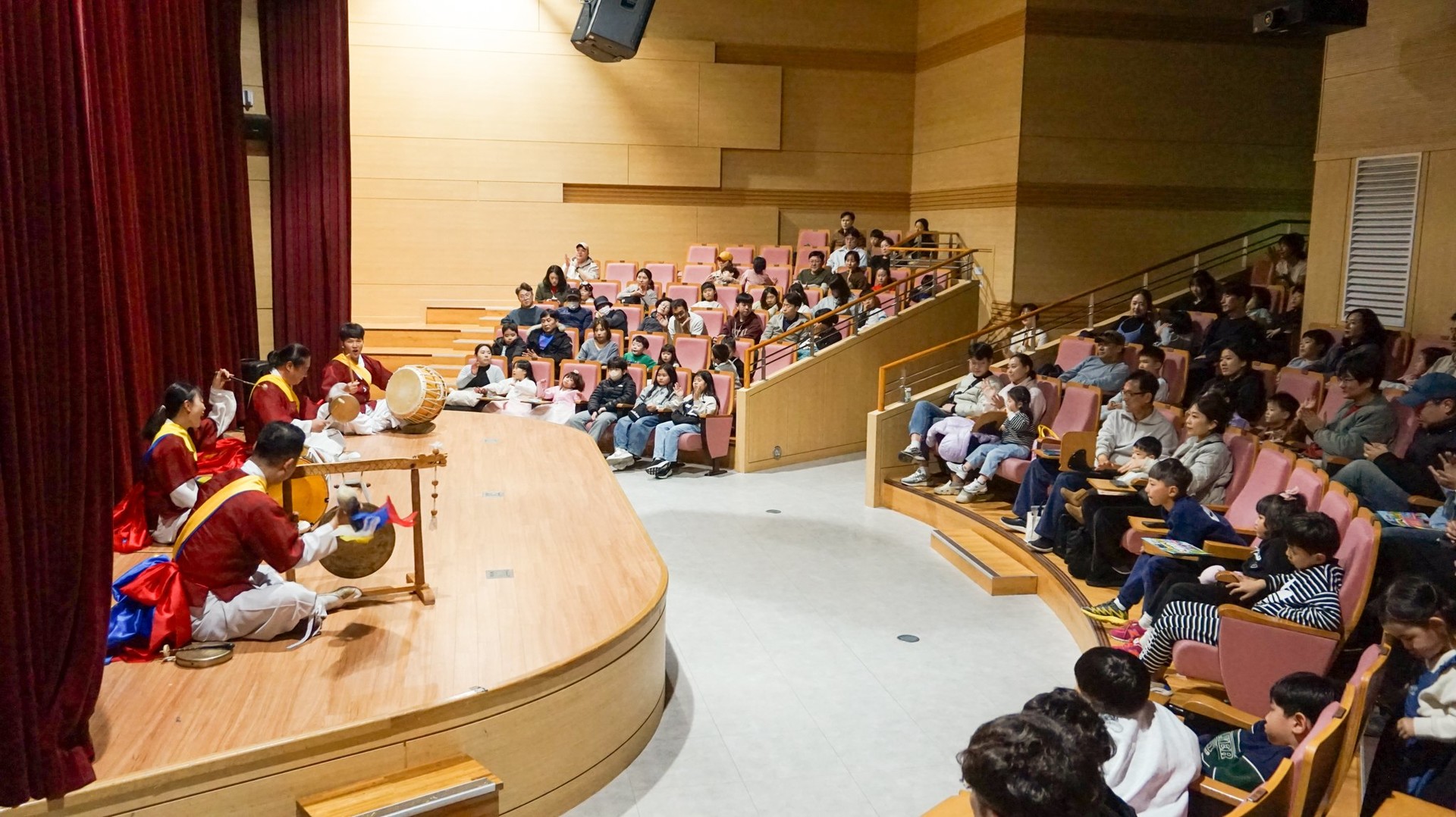 국립광주과학관 설날 특별 공연에서 합굿마을 연주자들이 역동적인 풍물놀이를 선보이고 있으며, 객석의 어린이와 부모님들이 입을 벌려 환호하고 즐거워하는 모습