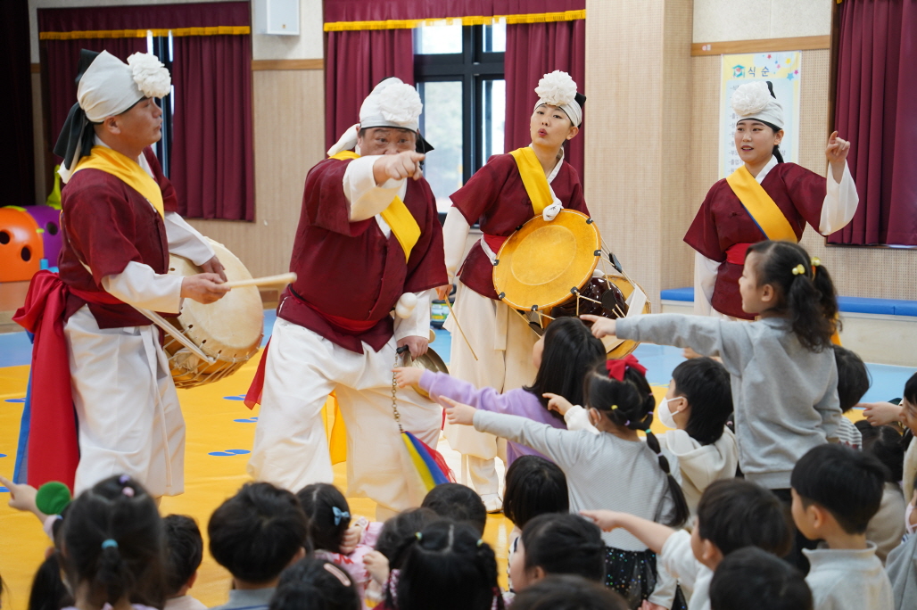 합굿마을 연희자들이 전주 푸른샘 유치원 아이들과 손가락으로 서로를 가리키며 유쾌하게 소통하는 모습. 공연자와 관객의 경계를 허물고 모두가 하나 되어 웃고 즐기는 풍물마당놀이 해피의 역동적인 쌍방향 공연 현장