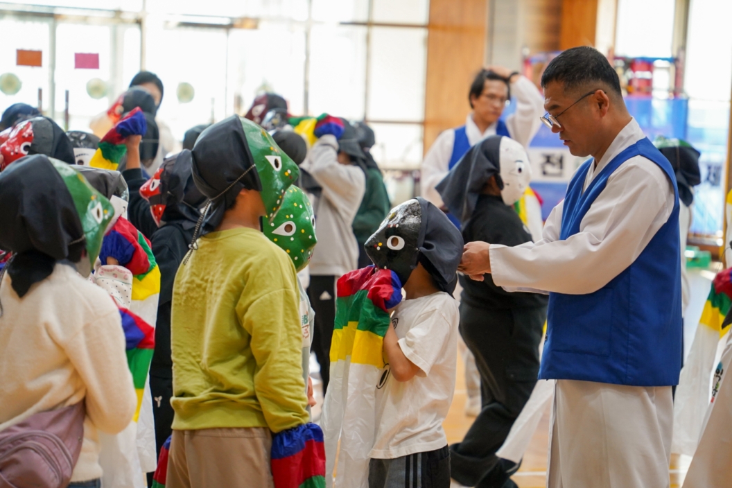전주 금암초 강당에서 합굿마을 강사가 아이에게 검은 탈을 씌워주며 체험을 돕는 모습