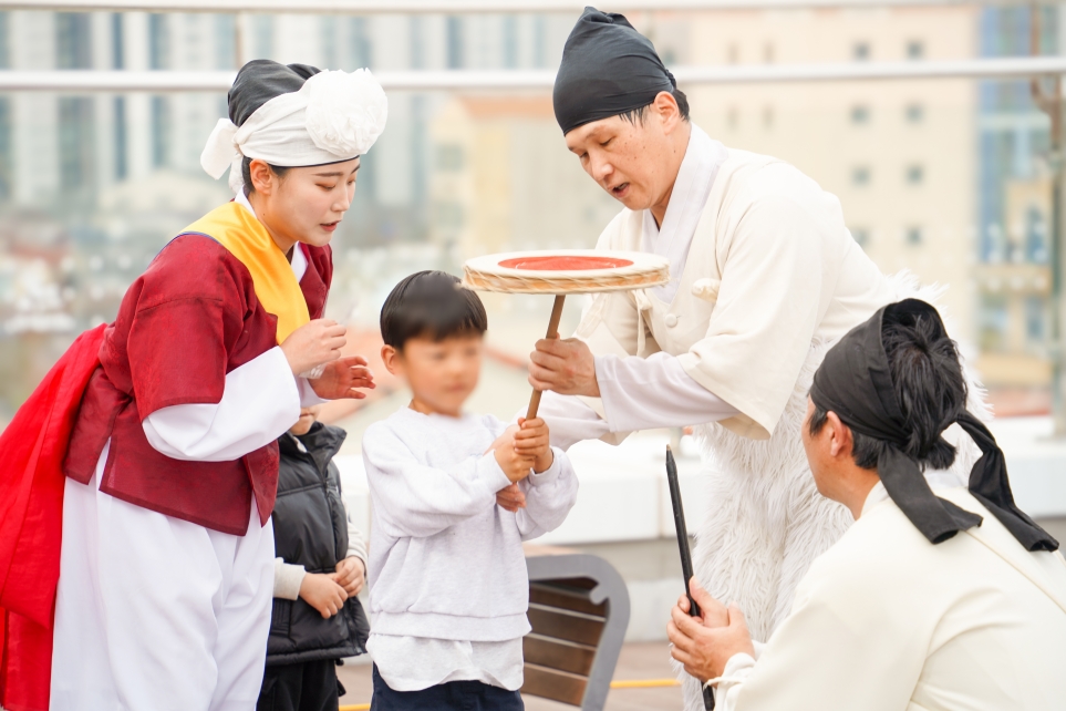 울산 강동바다도서관 옥상에서 초등학생 관객이 합굿마을 단원의 진지한 지도를 받으며 버나놀이(접시돌리기) 막대를 직접 잡고 균형을 잡아보는 전통문화 체험 현장