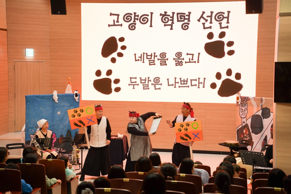 나는고양이로소이다 고양이 혁명 선언 장면 – 네발을 옳고 두발은 나쁘다 스크린과 피켓을 든 배우 3인, 합굿마을 세계명작동화 어린이마당놀이
