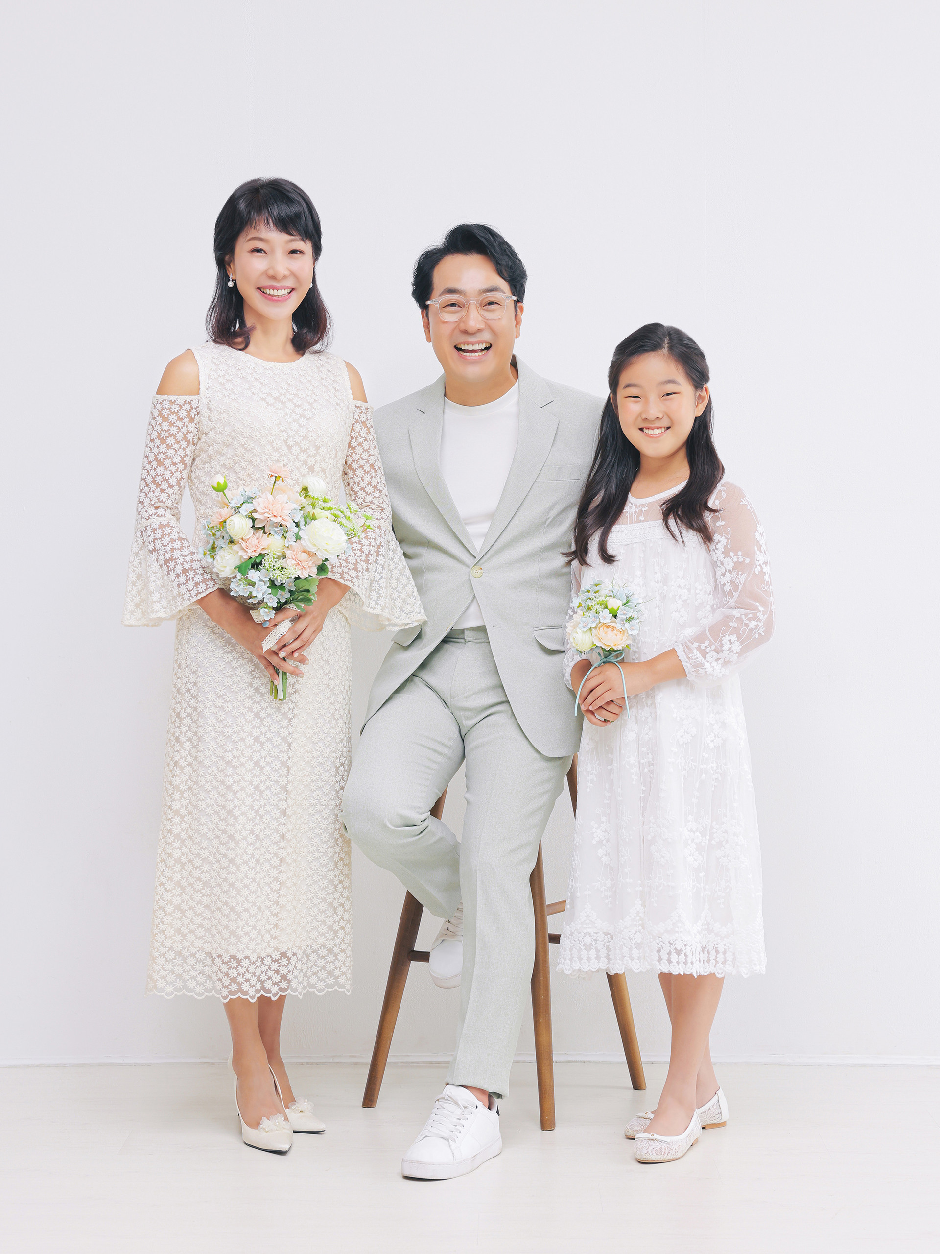 화이트 드레스와 밝은 정장으로 함께 웃는 세 가족의 사진