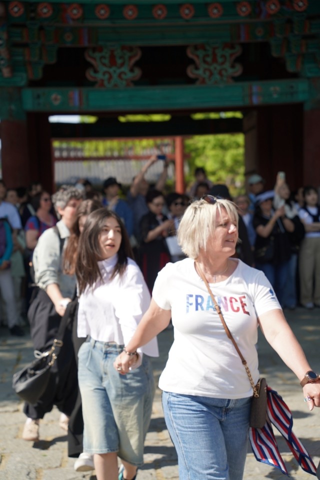 전주 한옥마을 전통연희 퍼레이드 대동놀이 마당에서 'FRANCE' 티셔츠를 입은 프랑스 관광객이 경기전 홍살문을 배경으로 손을 잡고 대동춤에 참여하는 장면. 수많은 관객들이 함께 어우러져 있다