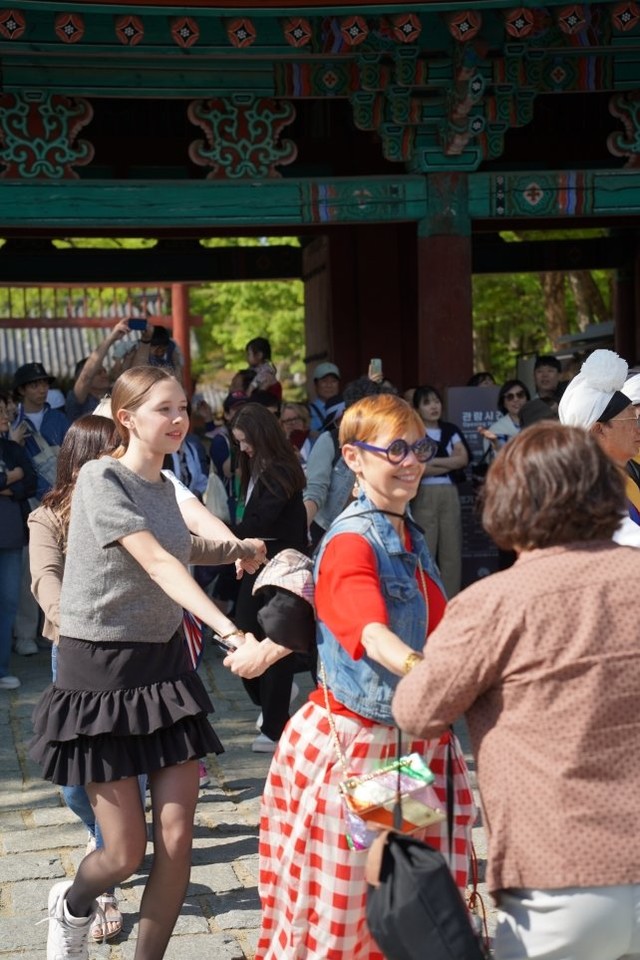전주 한옥마을 전통연희 퍼레이드 대동놀이 마당에서 경기전 홍살문을 배경으로 외국인 관광객들이 손을 잡고 함께 춤을 추는 장면. 서양인 모녀로 보이는 두 사람이 환하게 웃으며 대동의 흥에 빠져들고 있다