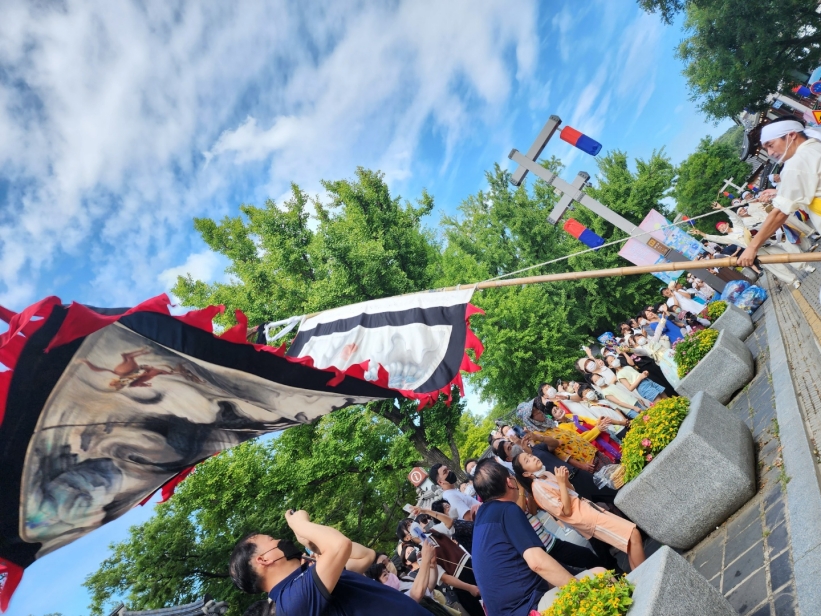 전주 한옥마을 전통연희 퍼레이드에서 전북무형문화재 전주기접놀이 용깃발이 하늘을 향해 펼쳐지는 장면. 수많은 관객들이 담장 위에서 공연을 지켜보고 있다