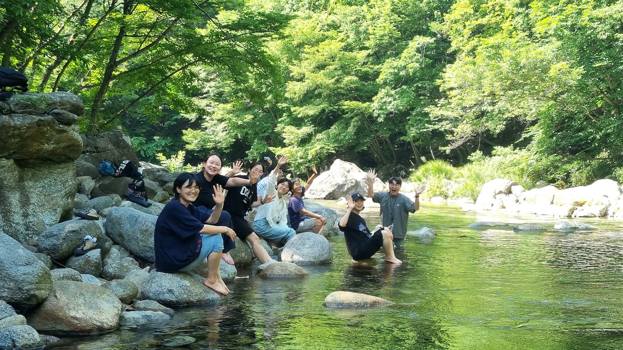 활동가들이 뱀사골 계울가에서 발을 담그며 카메라를 향해 손을 내밀고 웃고 있다