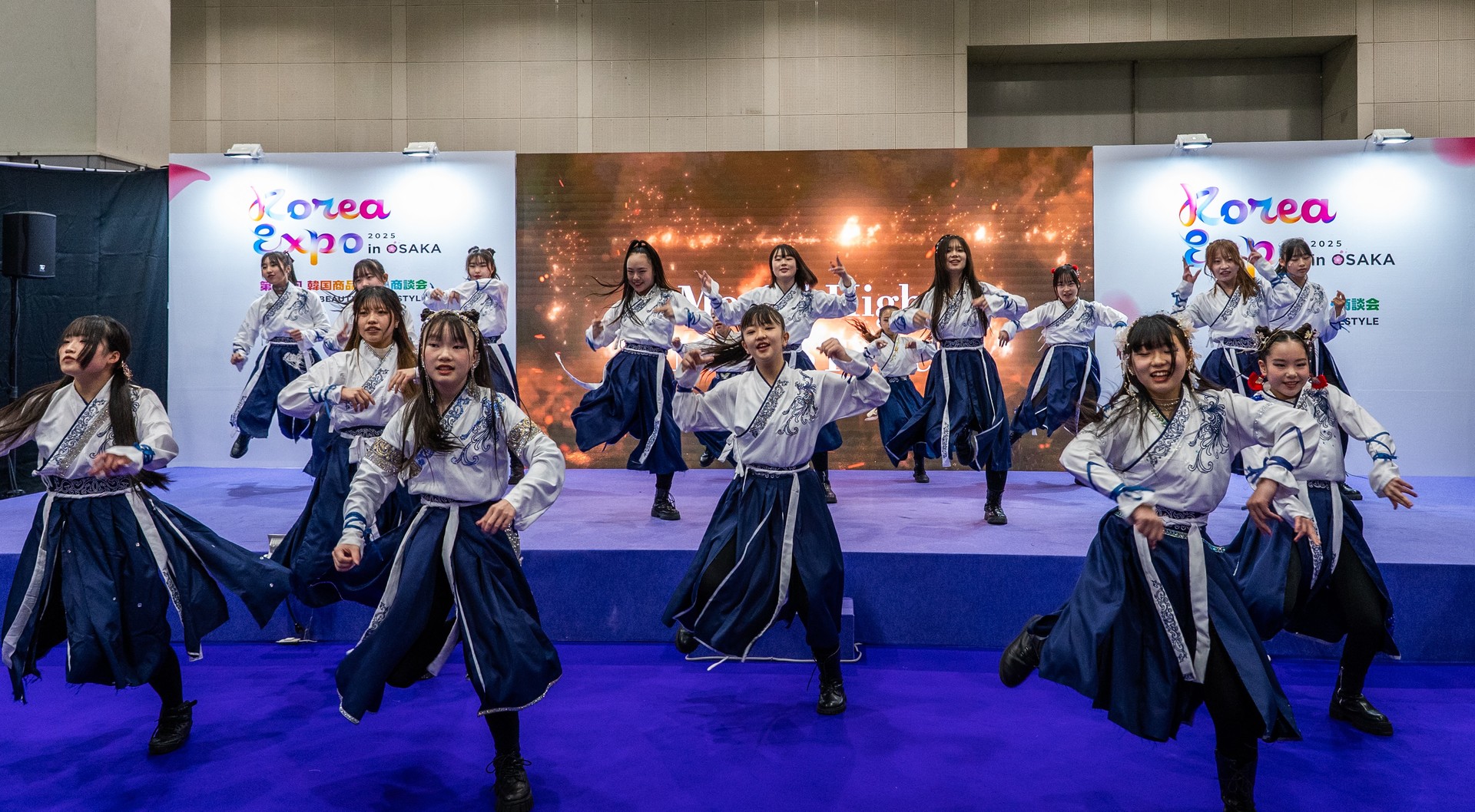 Performers in traditional-inspired costumes dance on stage during a Korea Expo live performance.