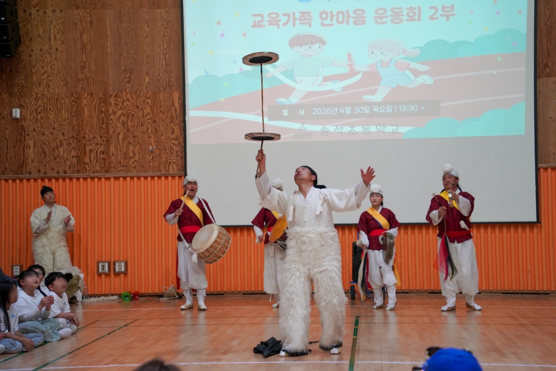 전통 접시 돌리기인 버나놀이를 선보이고 있다. 긴 막대 위에 두 개의 접시를 층으로 쌓아 올린 채 균형을 잡으며 돌리는 고난도 퍼포먼스와 이를 지켜보는 아이들의 놀라운 표정이 담긴 마당놀이 공연 현장