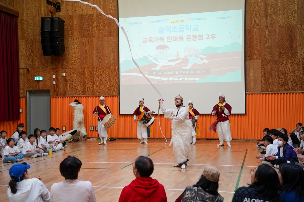 서천 송석초등학교 강당 무대에서 합굿마을 단원이 긴 줄을 돌리는 열두발 상모놀이 기예를 선보이고 있다. 허공에 화려한 곡선을 그리며 돌아가는 상모 줄과 이를 신기한 듯 바라보는 학생, 학부모들의 모습이 담긴 전통 마당놀이 공연 현장