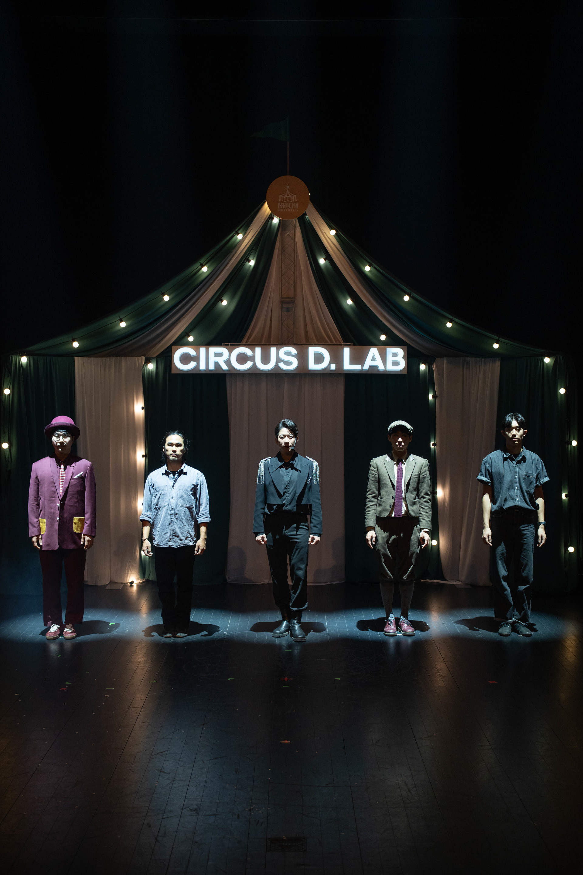 CIRCUS D.LAB 간판이 빛나는 어두운 무대에 선 다섯 단원