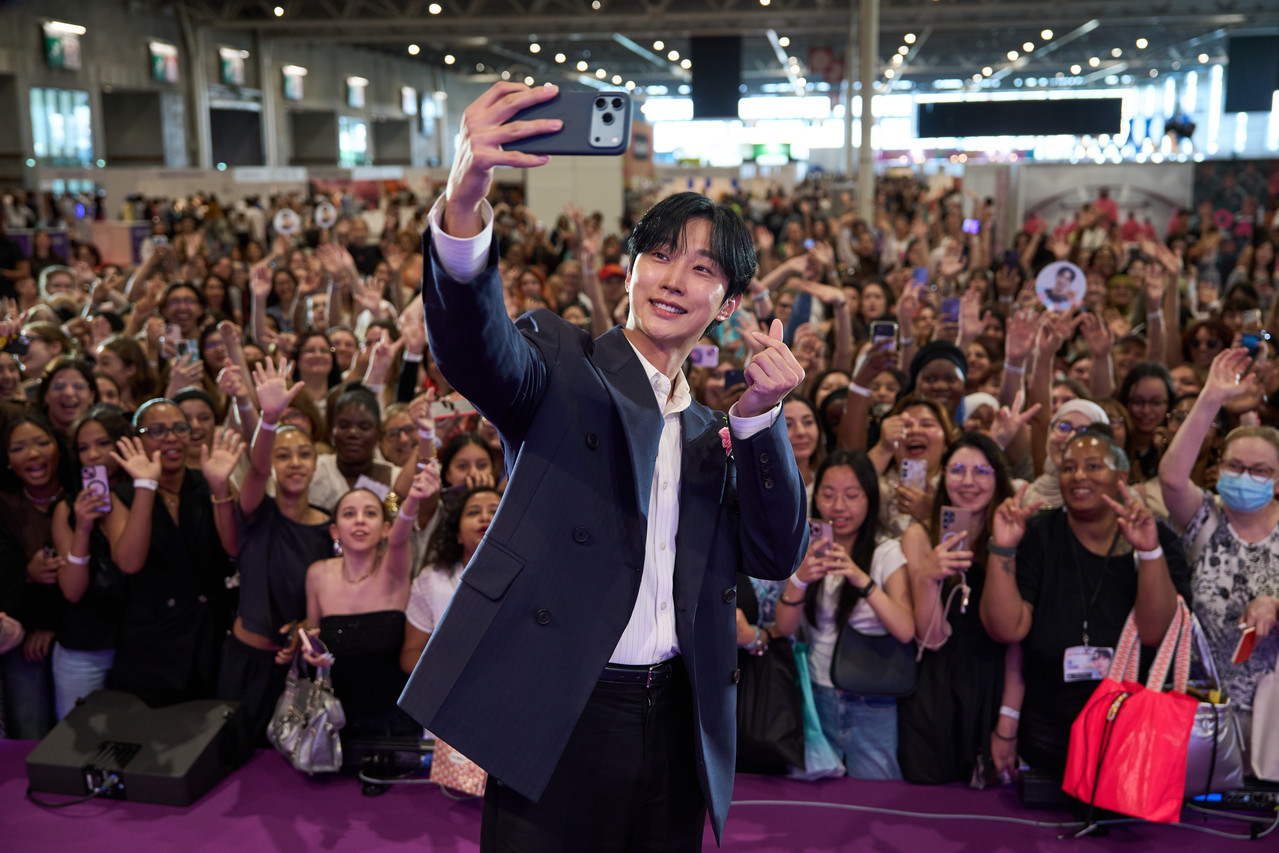 Visite surprise d'une célébrité coréenne lors de la Korea Expo 2025. Une fan prend un selfie avec un acteur coréen sur scène, montrant l'ambiance électrique